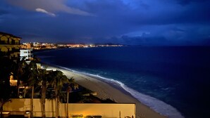 A coastal hotel with a beachfront view, a pool area, and a well-lit walkway along the beach.