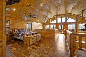 Une chambre à coucher dans une cabane en bois, avec un lit, une commode et une vue sur l’extérieur grâce à de grandes fenêtres.