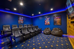 Une salle de cinéma avec des sièges en cuir noir, une moquette bleue ornée de motifs floraux jaunes et des affiches sur les murs.