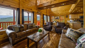 A wooden cabin with a balcony, furnished living room, and kitchen area. - New Construction Mountain Views, Hot Tub and Theater (Pigeon Forge)