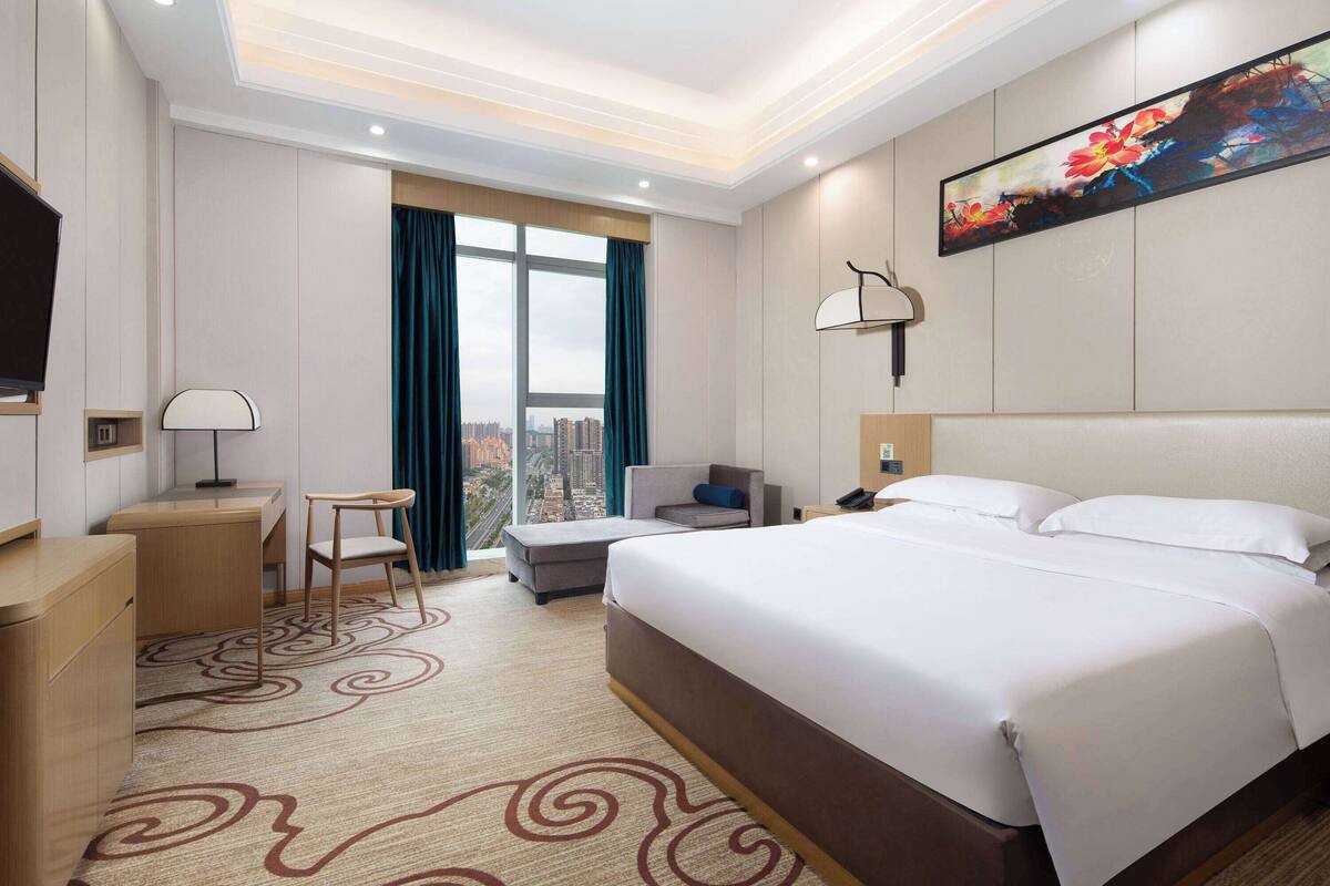 A hotel room with a large bed, a desk, a chair, a sofa, and a TV.