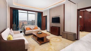 Una habitación de hotel moderna con sofá, una mesa de centro, televisor y un ventanal con vistas a la ciudad.