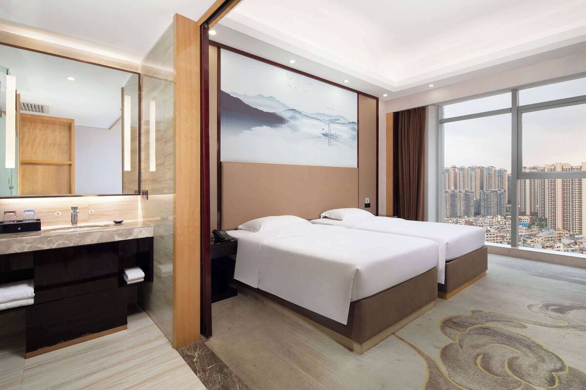 A hotel room with a bed, a desk, and a large window offering a city view.