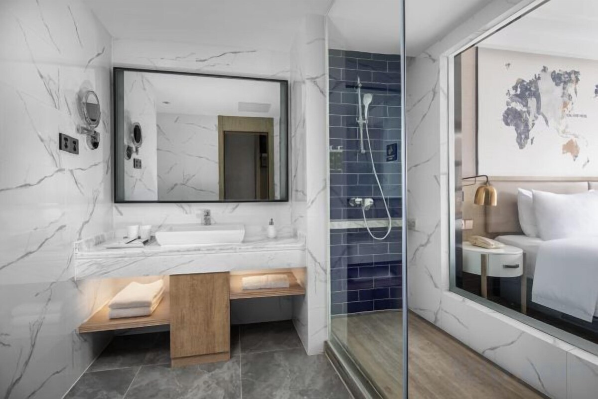 A modern bathroom with a marble vanity, a shower, and a bed with a view.