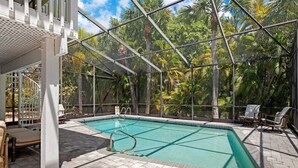 Una piscina con cerramiento de vidrio, rodeada de sillas de descanso y vistas a árboles tropicales.