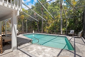 A swimming pool with a glass enclosure, surrounded by lounge chairs and a view of tropical trees. - Welcome to "Little Sanibel" 2/2 with Pool on East End Sanibel (Sanibel)