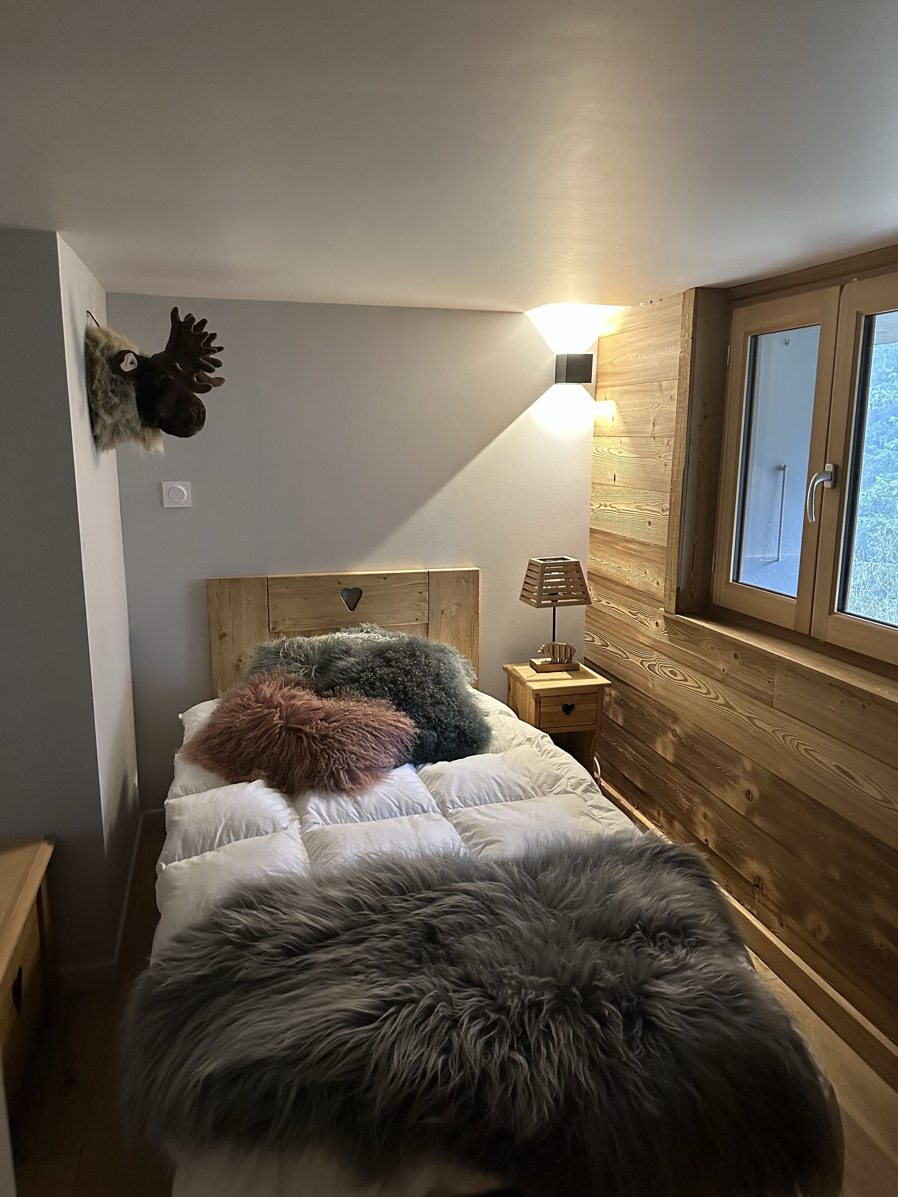 Une chambre confortable avec une tête de lit en bois, un lit moelleux agrémenté de plusieurs oreillers, une lampe de chevet et une tête de wapiti fixée au mur.