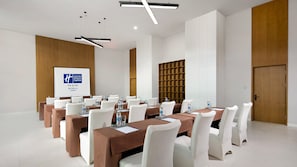 A conference room with multiple tables, white chairs, and a projection screen displaying a logo. - Holiday Inn Express Chongli (Zhangjiakou)