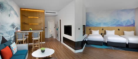 A hotel room with a sofa, two beds, a TV, a fireplace, and a dining area with chairs and a table.