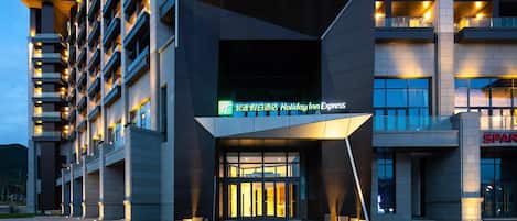 Una entrada de hotel moderna con un letrero de Holiday Inn Express, un amplio espacio de asientos al aire libre y un edificio de varios pisos con balcones.