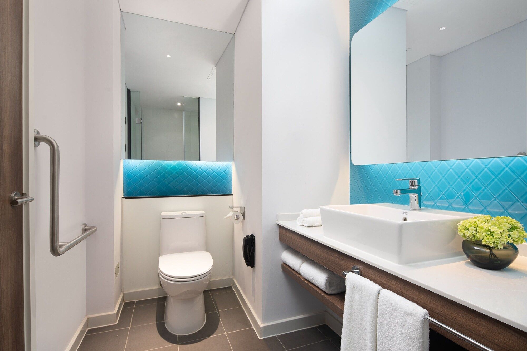 A modern bathroom with a white toilet, a sink with a blue backsplash, and a mirror above the sink.