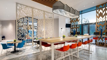 Un interior moderno con una mesa larga, sillas azules y rojas, y una pared decorativa con un diseño geométrico.