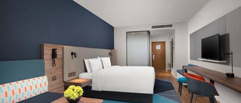 Une chambre d’hôtel avec un lit, un bureau, une télévision, un canapé et une petite table agrémentée de fleurs.