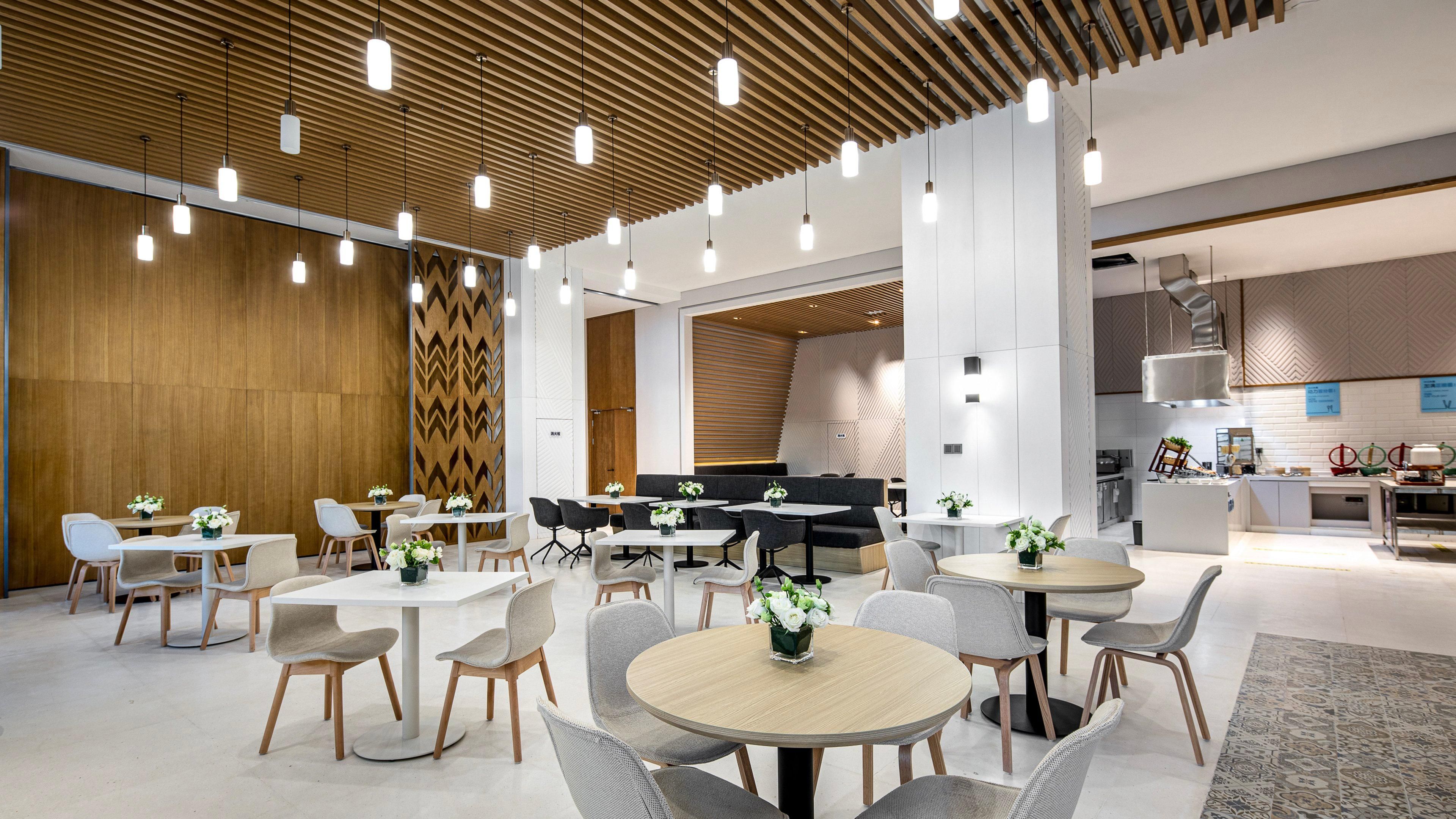 A modern dining area with round tables, grey chairs, and white flower centerpieces.