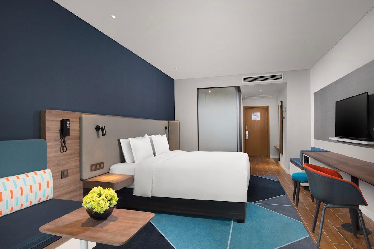 Habitación de hotel con cama, escritorio, televisor, sofá y una pequeña mesa con flores.