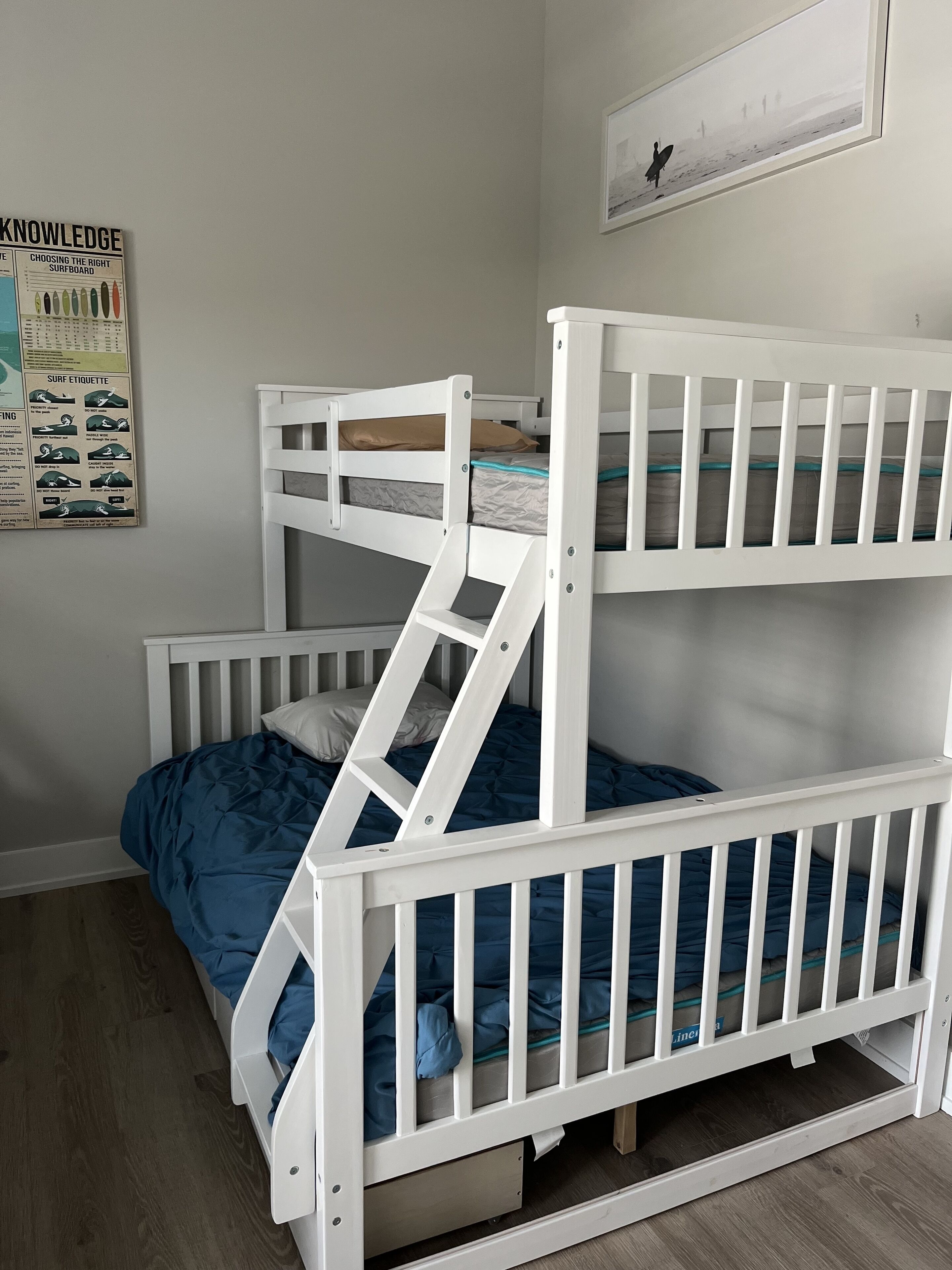 Una cama individual superpuesta con escalera, una colcha azul y un cartel en la pared.