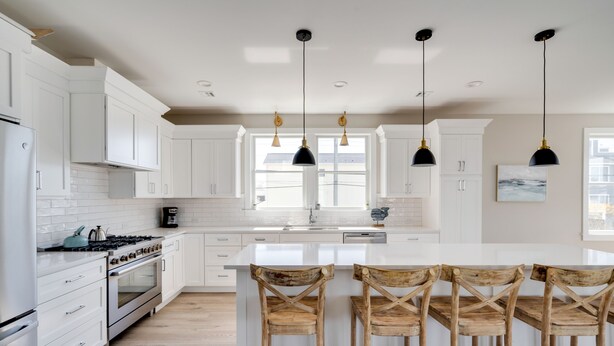 A modern kitchen with white cabinetry, a central island with bar stools, and pendant lighting. - SeaBreeze  (Surf City)