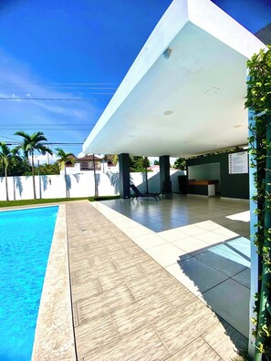 Un edificio moderno con zona de piscina, que incluye un espacio de descanso cubierto y vistas despejadas a la piscina.
