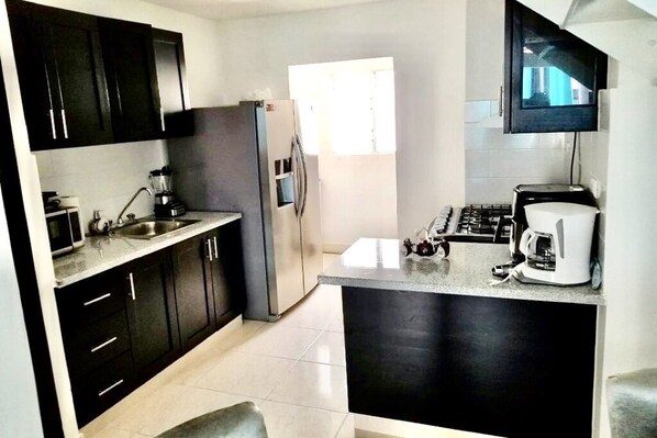 Una cocina moderna con armarios oscuros, un refrigerador de acero inoxidable, una cafetera y un televisor montado sobre la encimera.