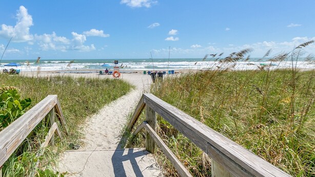 A wooden pathway leading to a beach with waves and a clear sky.