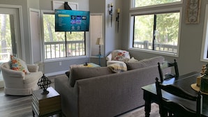 A living room with a large flat-screen TV, a sofa, a chair, and a table. - Creekside Cabin Under the Sycamores (Lake Montezuma)