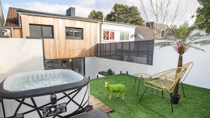 Un jacuzzi en un patio con césped artificial, una casa de madera y una palmera.