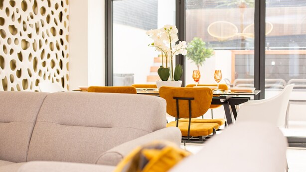 Un comedor moderno con un sofá, sillas amarillas y una mesa con un jarrón de flores blancas.