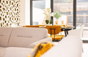 Un espace repas moderne avec un canapé, des chaises jaunes et une table agrémentée d’un vase de fleurs blanches.