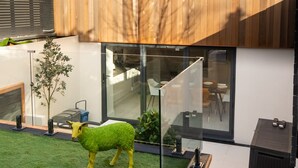 Una casa moderna con fachada de madera, puerta de cristal y un pequeño jardín con una escultura de oveja.