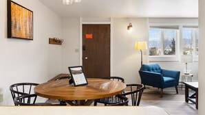 A dining area with a round wooden table, black chairs, a blue armchair, a lamp, and a framed picture on the table. - Outpost: Gros Ventre B9 - Hot Tub Access (Teton Village)