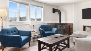 A living room with two blue armchairs, a wooden coffee table, a fireplace, and a view of mountains through large windows. - Outpost: Gros Ventre B9 - Hot Tub Access (Teton Village)