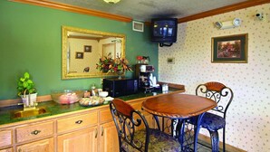 A dining area with a wooden table and chairs, a green wall, a mirror, a television, and a coffee machine.