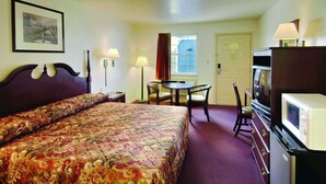 A hotel room with a large bed, a desk with a chair, a television, and a window with curtains.