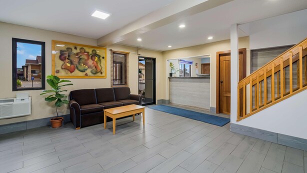 A reception area with a sofa, a coffee table, a potted plant, a painting, and a staircase. - Americas Best Value Inn Fargo (Fargo)