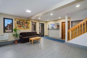 A reception area with a sofa, a coffee table, a potted plant, a painting, and a staircase. - Americas Best Value Inn Fargo (Fargo)