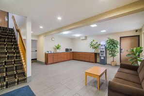 Vestíbulo de hotel con escalera, mostrador de recepción, sofá, mesa y zona de cocina.
