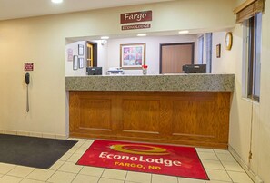 Un mostrador de recepción con un cartel de Fargo EconoLodge, un teléfono, cuadros enmarcados y una alfombra roja con el logotipo del hotel.