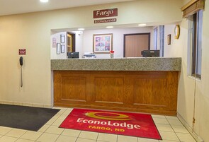 Un mostrador de recepción con un cartel de Fargo EconoLodge, un teléfono, cuadros enmarcados y una alfombra roja con el logotipo del hotel.