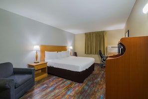 Ein Hotelzimmer mit Bett, Nachttisch, Lampe, Stuhl, Schreibtisch und Klimaanlage.