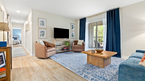Un salon moderne avec une table basse en bois, deux canapés, un téléviseur et une grande fenêtre avec des rideaux.