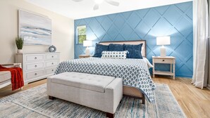 Une chambre à coucher comprenant un lit, des tables de chevet, un ventilateur de plafond, un banc et un tapis.