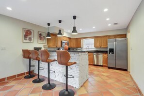 Una cocina moderna con una isla central, taburetes de bar, electrodomésticos de acero inoxidable y armarios de madera.