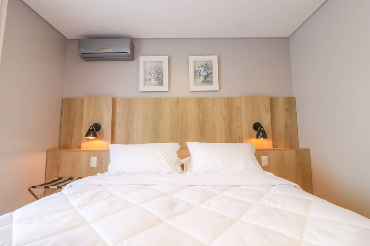 A neatly made bed with a quilted white duvet, two bedside lamps, and a wooden headboard.
