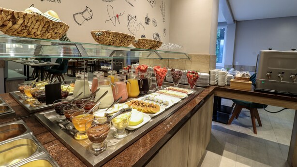 A buffet with various food items and beverages, a wall with food illustrations, and a seating area with tables and chairs. - Pousada Bella Viena (Gramado)