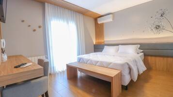 A modern hotel room with a bed, a desk, a bench, and a large window with curtains.