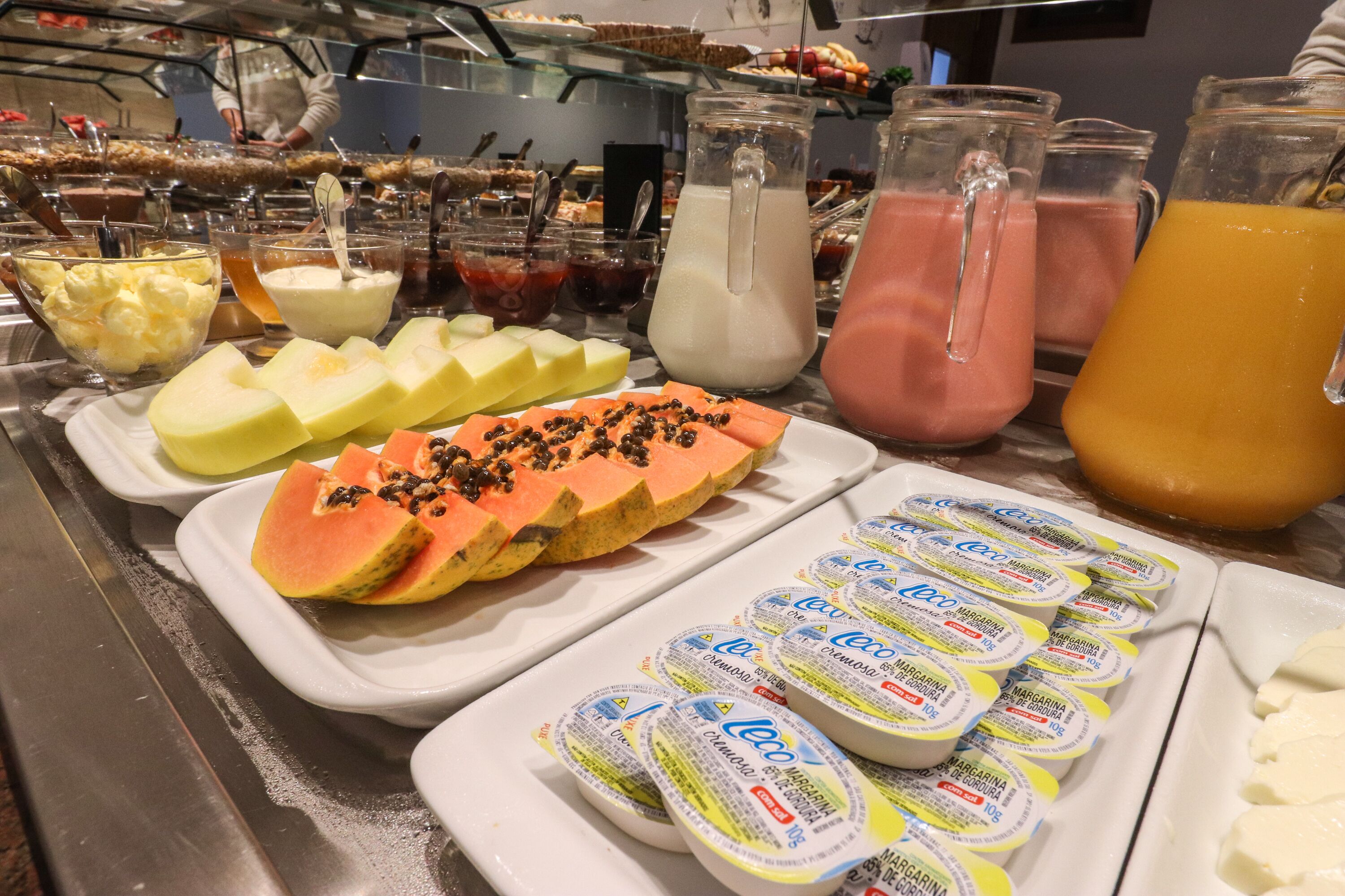 A buffet with various food items including sliced fruits, yogurt, and beverages.