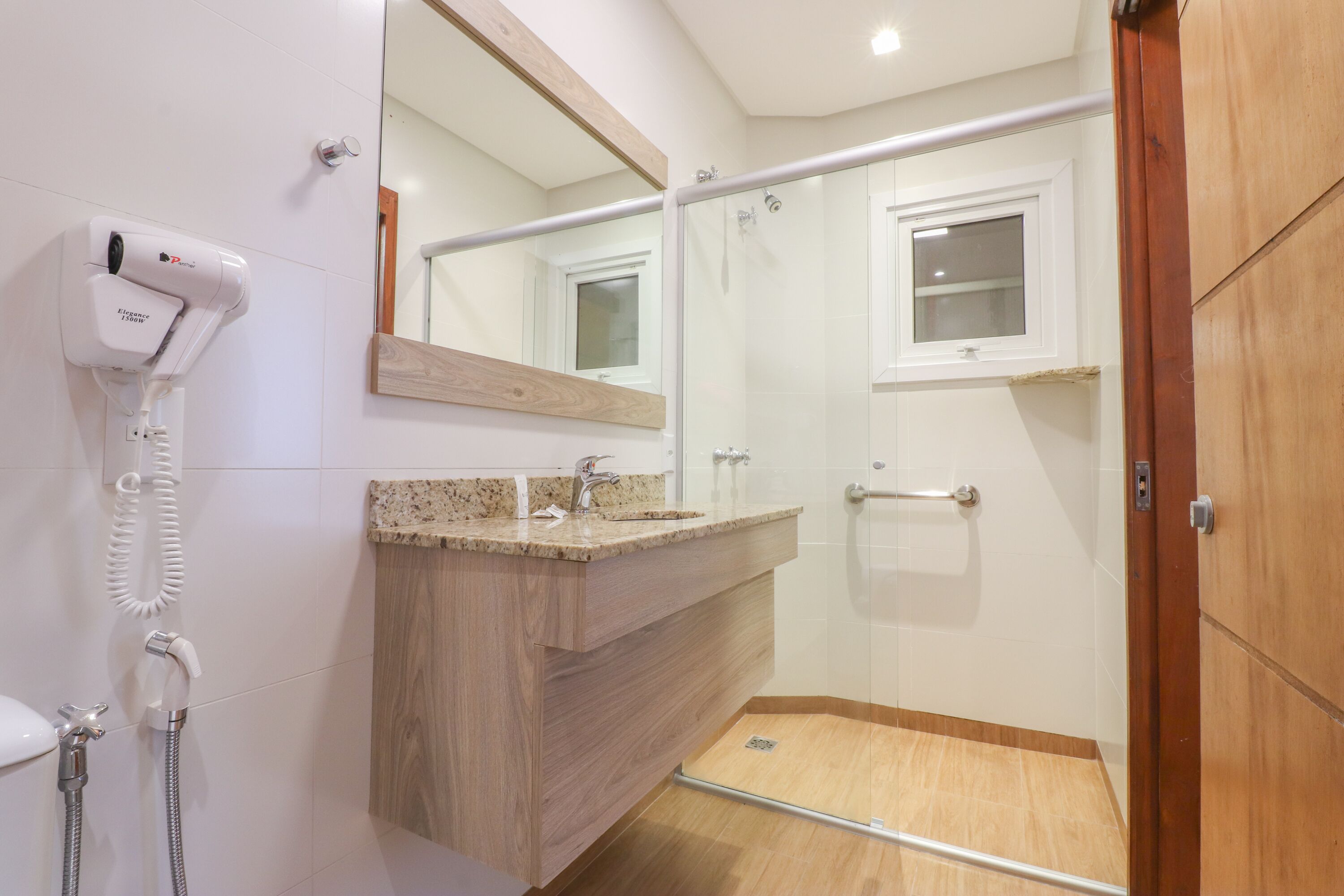 A modern bathroom with a hairdryer, a sink, a mirror, and a shower area.