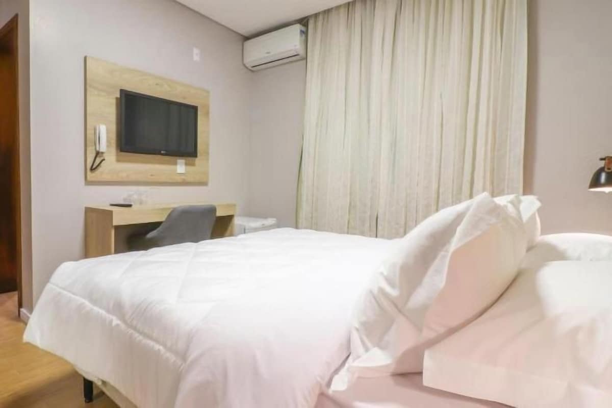 Una habitación de hotel con cama, escritorio, silla, televisor y armario.