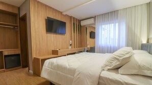 A hotel room with a large bed, wooden wardrobe, TV, and air conditioning unit. - Pousada Bella Viena (Gramado)