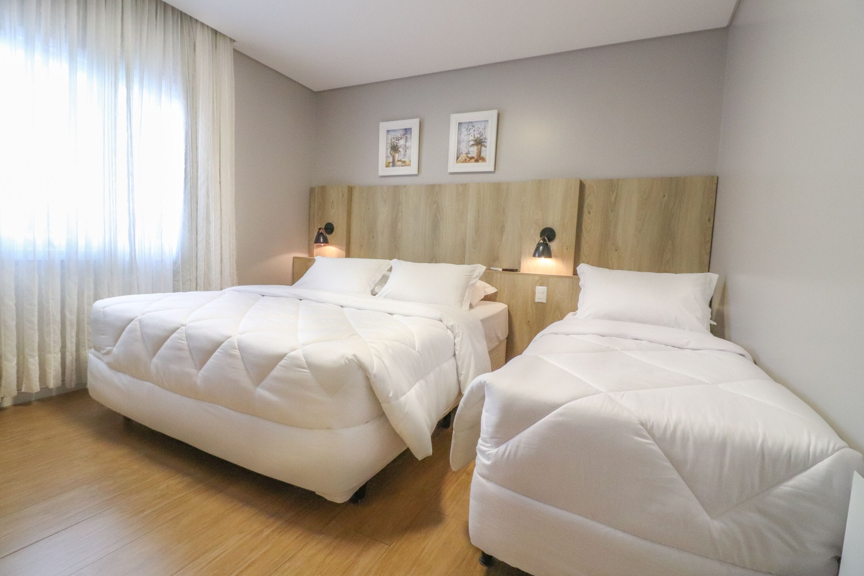 A hotel room with two beds, wooden headboard, and two wall-mounted lamps.
